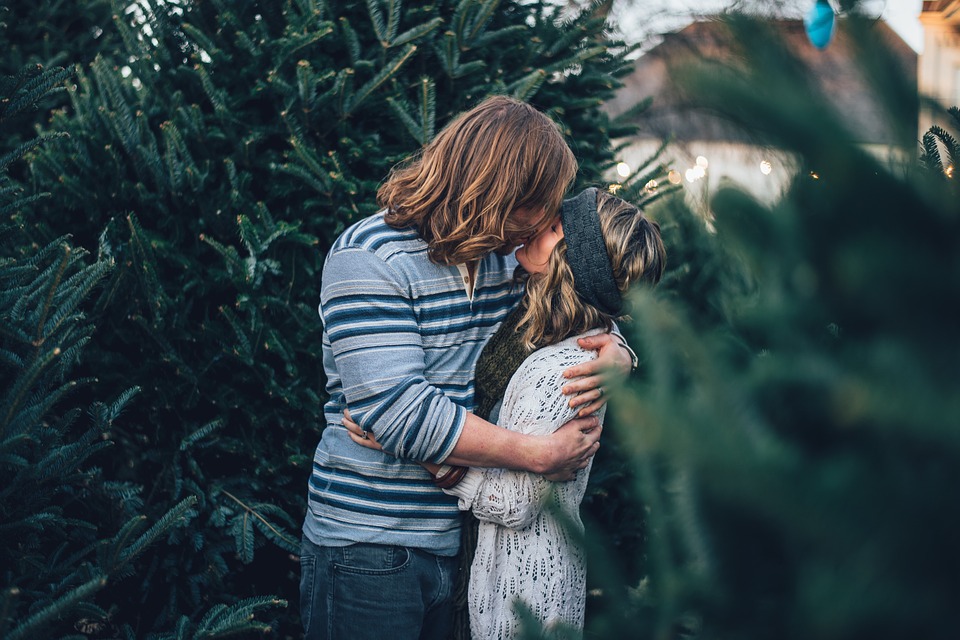 Man and woman kissing each others lips beside a tree.